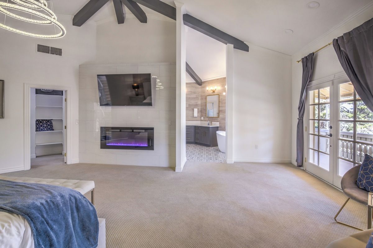 A spacious bedroom with a large bed, a fireplace, and a view of the balcony.