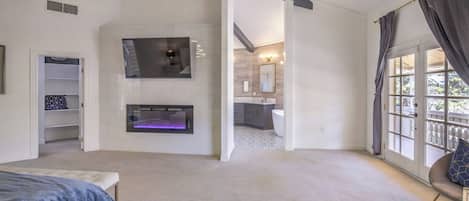 A spacious bedroom with a large bed, a fireplace, and a view of the balcony.