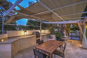 Eine Außenpatio mit Holztisch und -stühlen, einem Grill und einer Steinsäule.