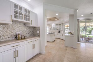 A modern kitchen with white cabinetry, a stone backsplash, and a central island. - 5700 sqft Lux Golf Villa w Pool & Spa Near Strip (Henderson)