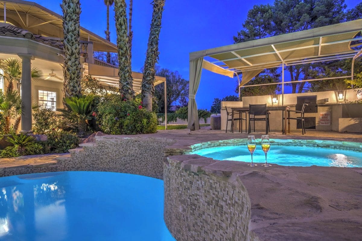 Uma área de piscina com espaço de estar coberto, um bar e vista para um edifício junto à piscina.