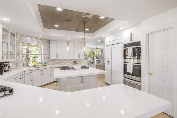 A modern kitchen with white cabinetry, a central island, stainless steel appliances, and pendant lighting. - 5700 sqft Lux Golf Villa w Pool & Spa Near Strip (Henderson)