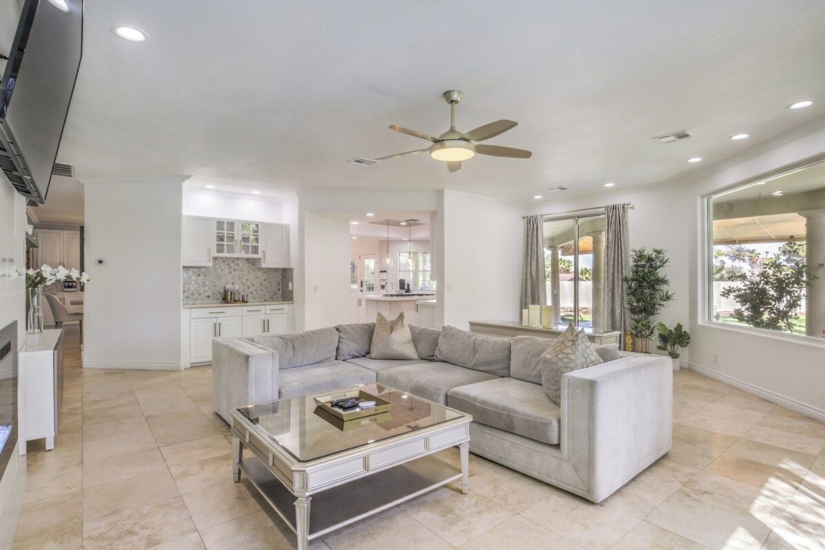 A spacious living room with a sectional sofa, a glass coffee table, and a ceiling fan.