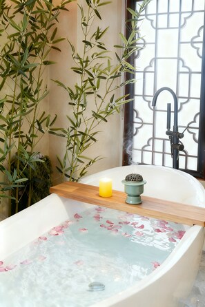 Une baignoire remplie de pétales de rose, une bougie et un petit objet décoratif posé sur une étagère en bois.
