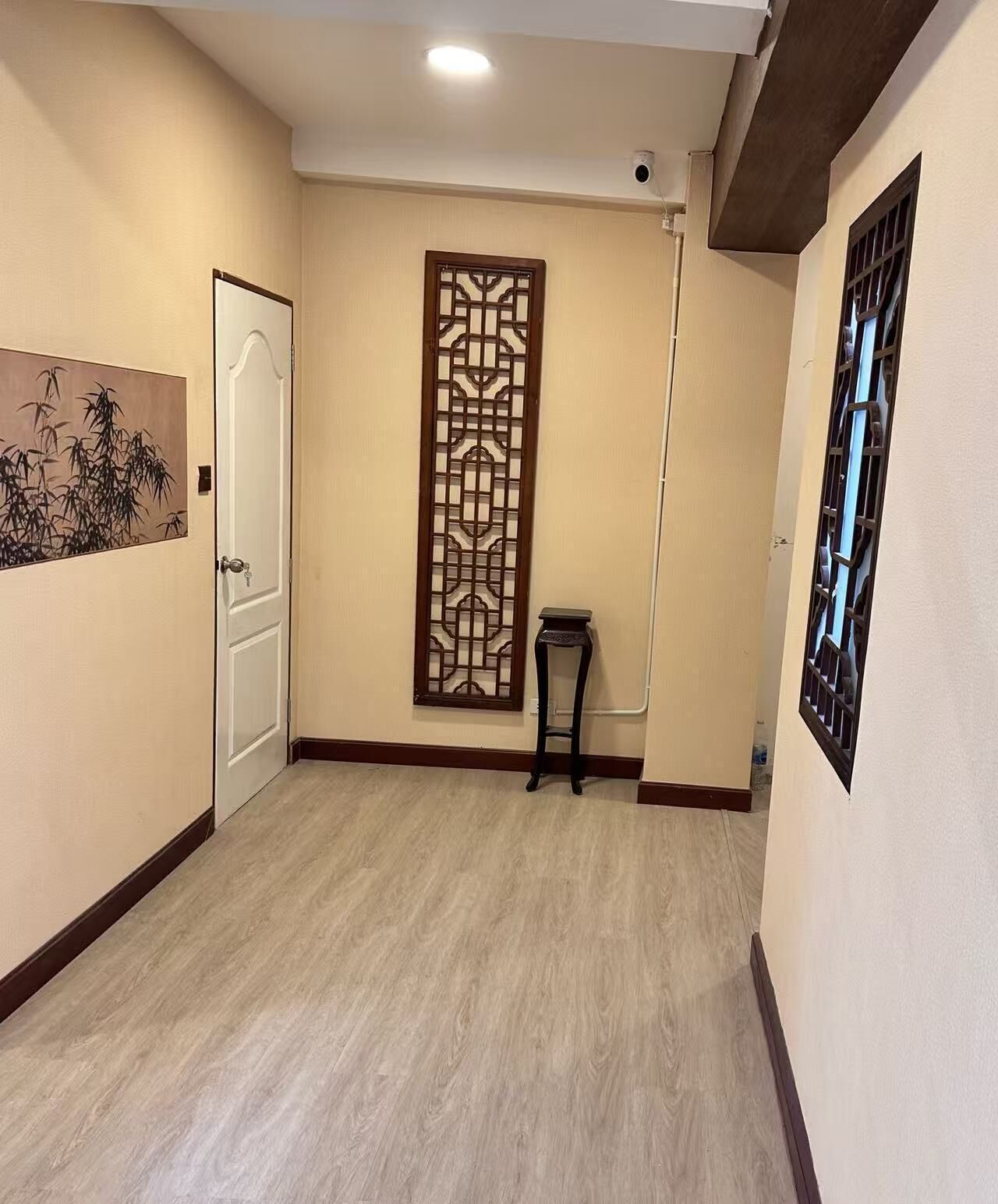 A hallway with a wooden floor, a decorative panel, a door, and a small table.