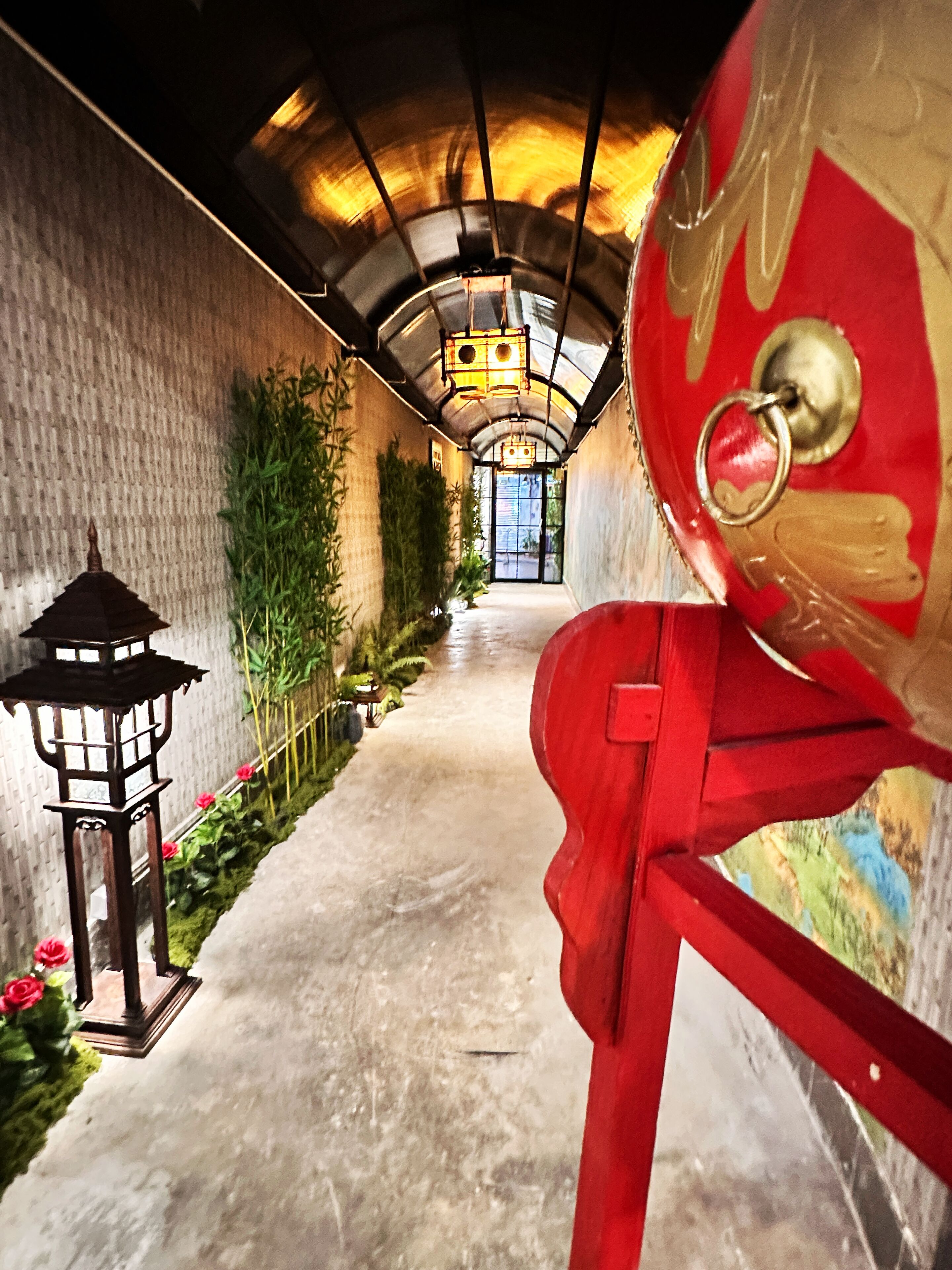 A corridor with a red sculpture, a lantern, and bamboo plants.