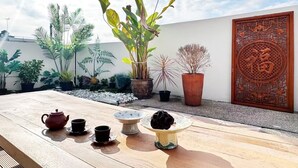 Un jardín en la azotea con plantas en macetas, una mesa de madera con juego de té y una puerta decorativa.