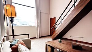 Una sala de estar moderna con un sofá, cojines, una mesa de centro, una lámpara y una escalera.