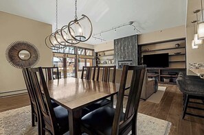 Een eetgedeelte met een houten tafel en stoelen, een kroonluchter en een grote spiegel aan de muur.