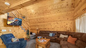 Ein gemütliches Blockhaus-Interieur mit blauem Liegesessel, braunem Ledersofa und einem Holztisch.