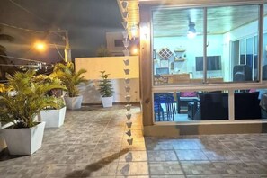 Una terraza en la azotea con plantas en macetas, suelo de baldosas y vistas del interior a través de amplias ventanas.