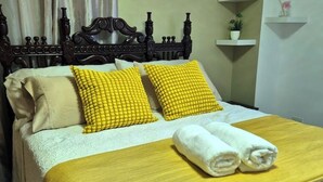 Una cama bien hecha con una colcha amarilla, dos almohadas amarillas y un par de toallas blancas.