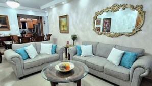 Una sala de estar con dos sofás grises, una mesa de centro de vidrio y un comedor al fondo.