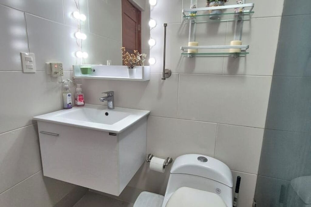 Une salle de bain avec un lavabo blanc, un miroir avec éclairage intégré et des toilettes.