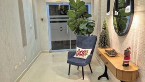 Un pasillo moderno con una silla gris, un pequeño árbol de Navidad y un espejo decorativo en la pared.