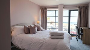 Een hotelkamer met een groot bed, een bureau en uitzicht op de stad door grote ramen.