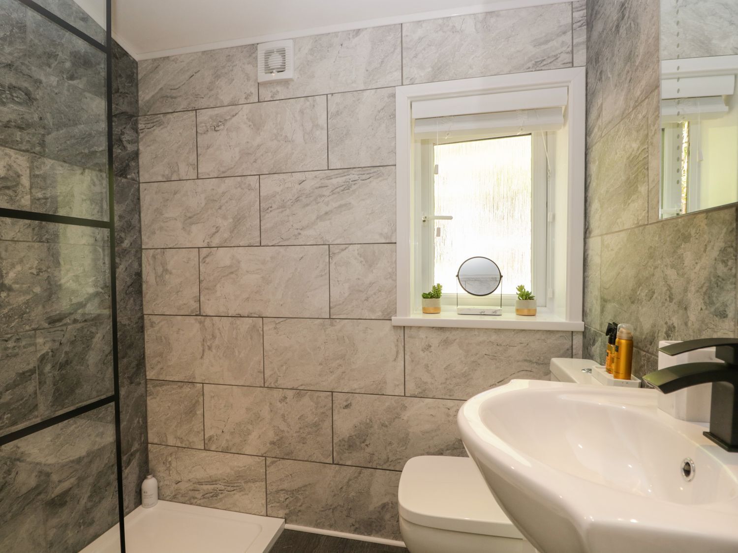 A bathroom with a white sink, a toilet, and a window with a mirror.