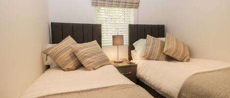 A twin room with two beds, a nightstand, a lamp, and a window with blinds.