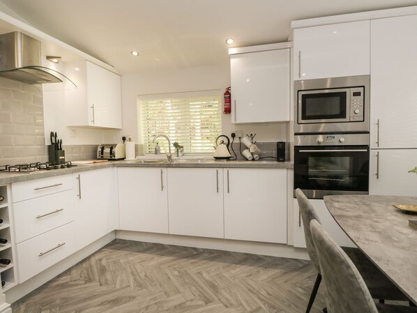 Una cocina moderna con gabinetes blancos, electrodomésticos de acero inoxidable y un suelo de madera con diseño de espiga.