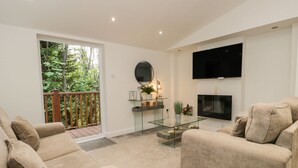 Una sala de estar con una mesa de centro de vidrio, sofás color beige, una chimenea y un televisor montado en la pared.