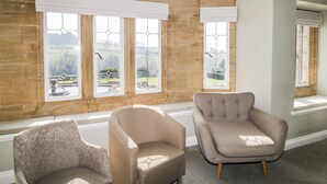 A room with two armchairs, large windows with white valances, and a view of a park. - Harcombe House Rooms - First Floor Single (Newton Abbot)