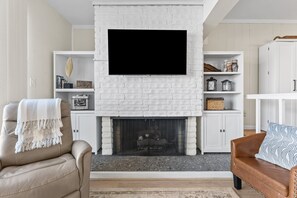 Un salón con chimenea de ladrillo blanco, televisor montado y mobiliario de cuero.