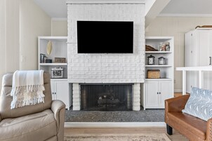 Un salón con chimenea de ladrillo blanco, televisor montado y mobiliario de cuero.