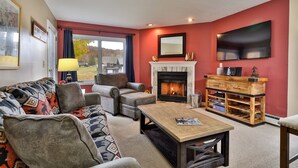 A living room with a fireplace, a sofa set, a coffee table, and a TV mounted on the wall. - Pico Mountain Condo F106 3 Bedroom Home (Killington)