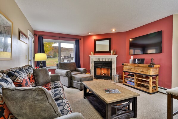 A living room with a fireplace, a sofa set, a coffee table, and a TV mounted on the wall. - Pico Mountain Condo F106 3 Bedroom Home (Killington)