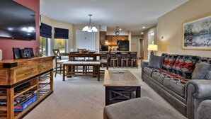 A living room with a TV, wooden furniture, a sofa, and a dining area with chairs and a table. - Pico Mountain Condo F106 3 Bedroom Home (Killington)