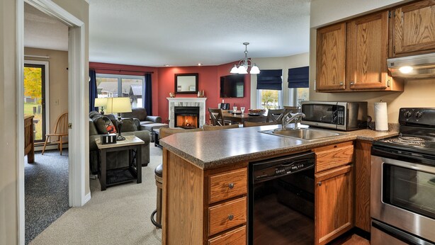 A modern kitchen with wooden cabinets, a dishwasher, a stove, and a microwave. - Pico Mountain Condo F106 3 Bedroom Home (Killington)