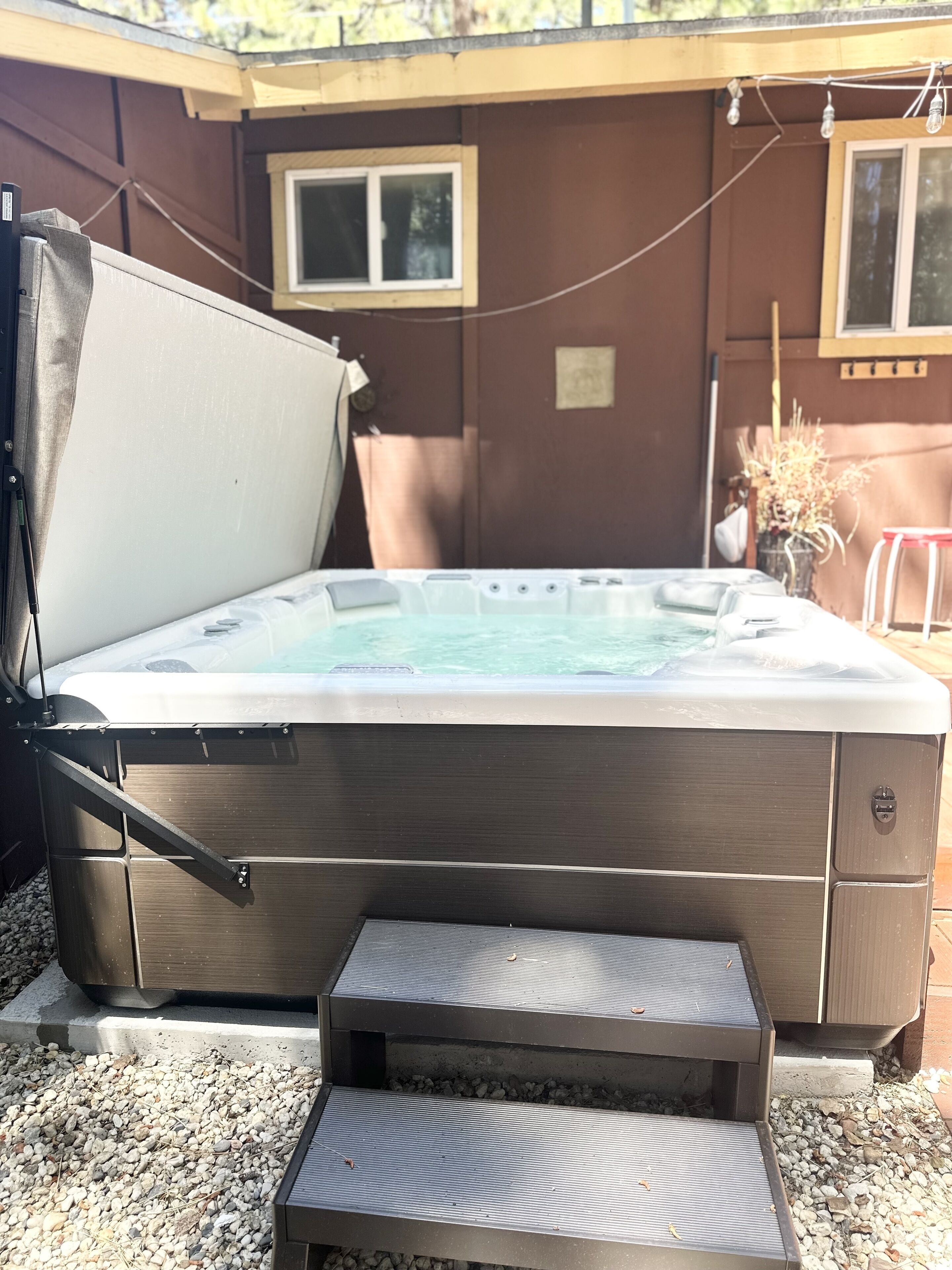 A hot tub with steps leading up to it, set against a wooden wall with windows.