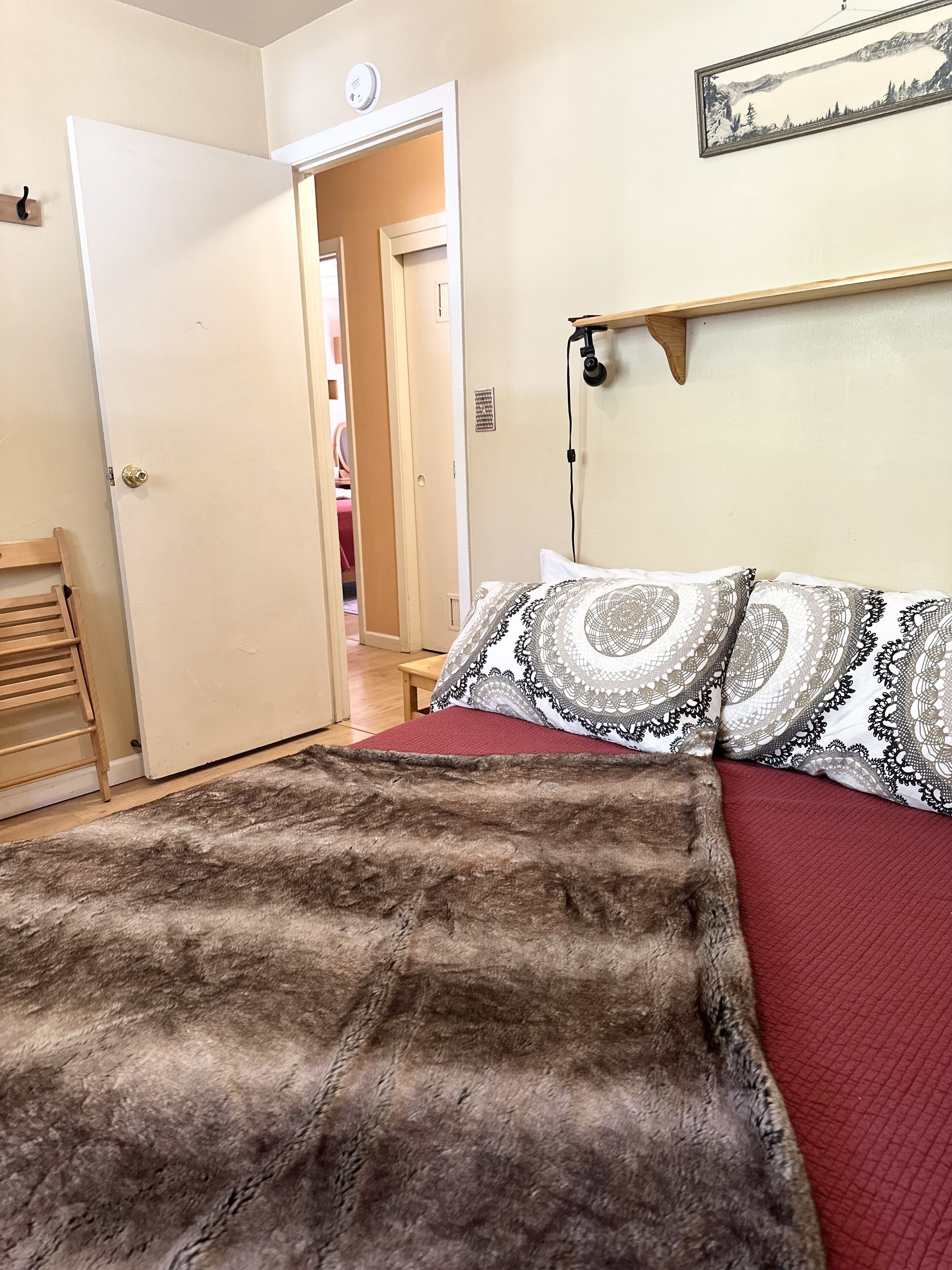 A bedroom with a bed, a wooden ladder, a door, and a wall-mounted light fixture.