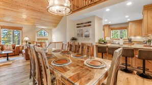A spacious dining area with a large wooden table, surrounded by chairs, and a kitchen area with wooden cabinets and a bar. - Woodlands House 3 Bedroom Home (Truckee)
