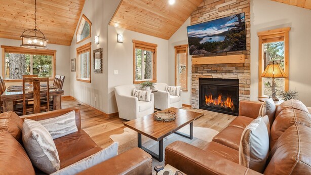 A spacious living room with a fireplace, leather sofas, and a dining area with a wooden table and chairs. - Woodlands House 3 Bedroom Home (Truckee)