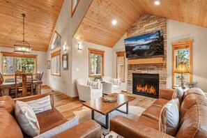 A spacious living room with a fireplace, leather sofas, and a dining area with a wooden table and chairs. - Woodlands House 3 Bedroom Home (Truckee)