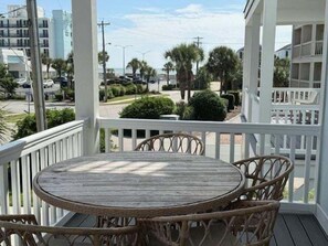 A wooden table and wicker chairs on a porch with a view of a street and buildings. - Sea Pearl 7 Bedroom Home (Surfside Beach)