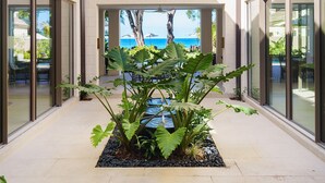 A modern hotel corridor with large glass doors, a water feature, and a view of the ocean. - Sea Grove House 5 Bedroom Villa (Weston)