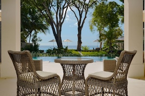 Wicker furniture near a pool with a view of the ocean and palm trees. - Sea Grove House 5 Bedroom Villa (Weston)