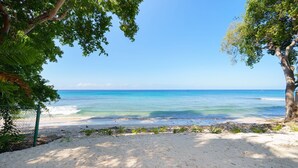 A beach with clear turquoise water, sandy shore, and trees providing shade. - Sea Grove House 5 Bedroom Villa (Weston)