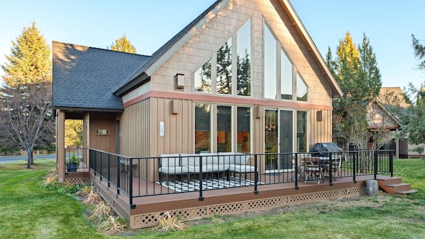 Ein modernes Haus mit einer großen Terrasse, einer überdachten Veranda und einem markanten Giebeldach.