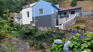 A house with a blue and white exterior, a stone pathway, and surrounding greenery. - House of Rising Sun (Remédios, Ponta Delgada)