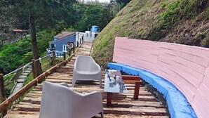 A wooden deck with a table and chairs, a blue-painted wall, and a staircase leading uphill. - House of Rising Sun (Remédios, Ponta Delgada)