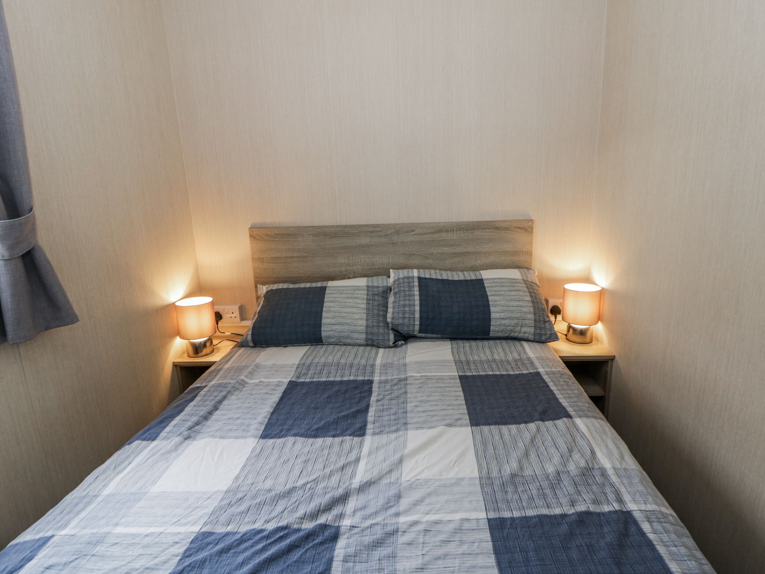 Un lit bien fait, avec une couvre-lit à carreaux, deux lampes de chevet et une tête de lit en bois.