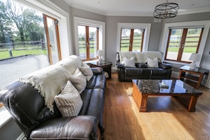 A spacious living room with leather sofas, a marble coffee table, and large windows offering a view of the outdoors.