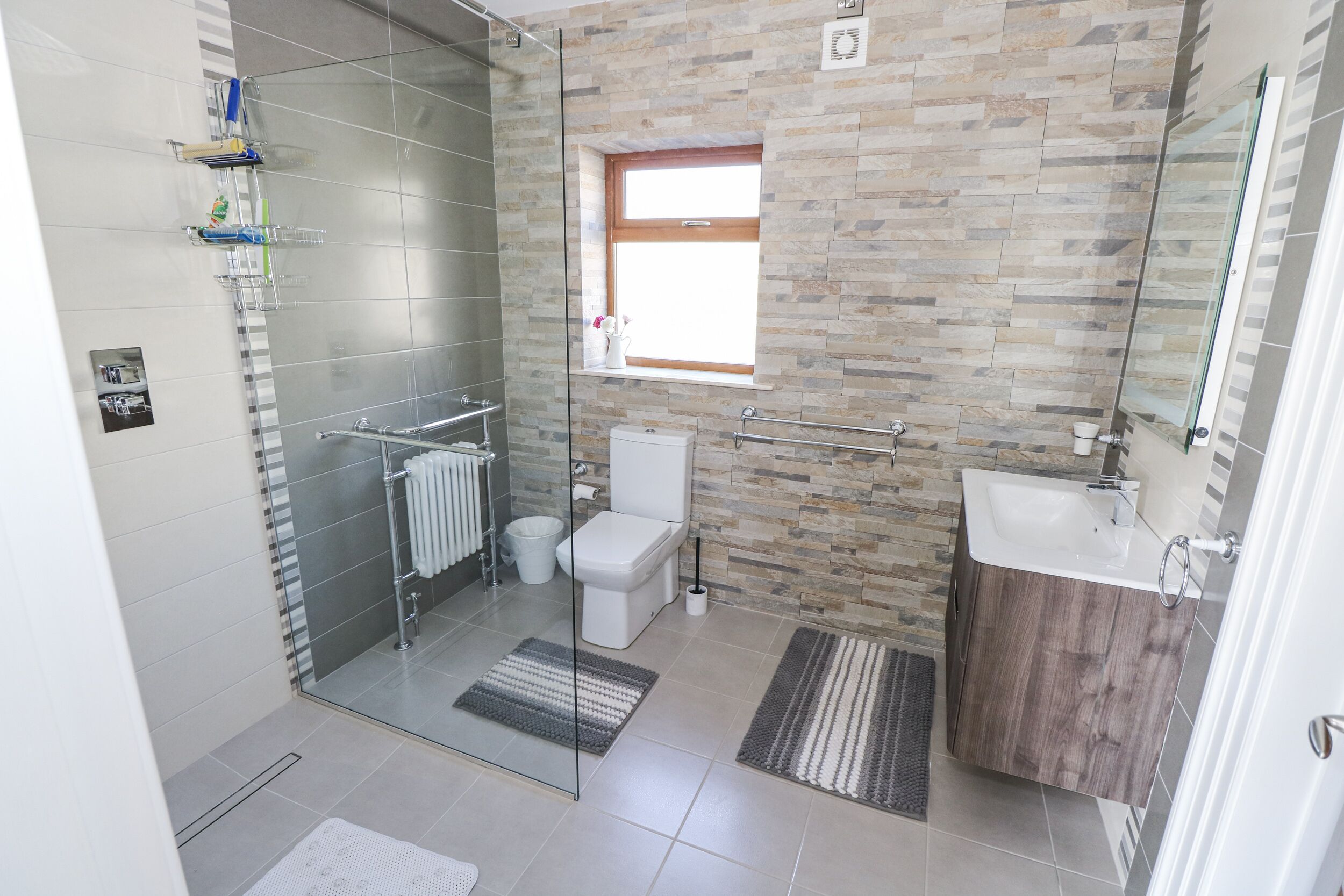 A modern bathroom with a glass shower enclosure, a toilet, a sink, and a window.