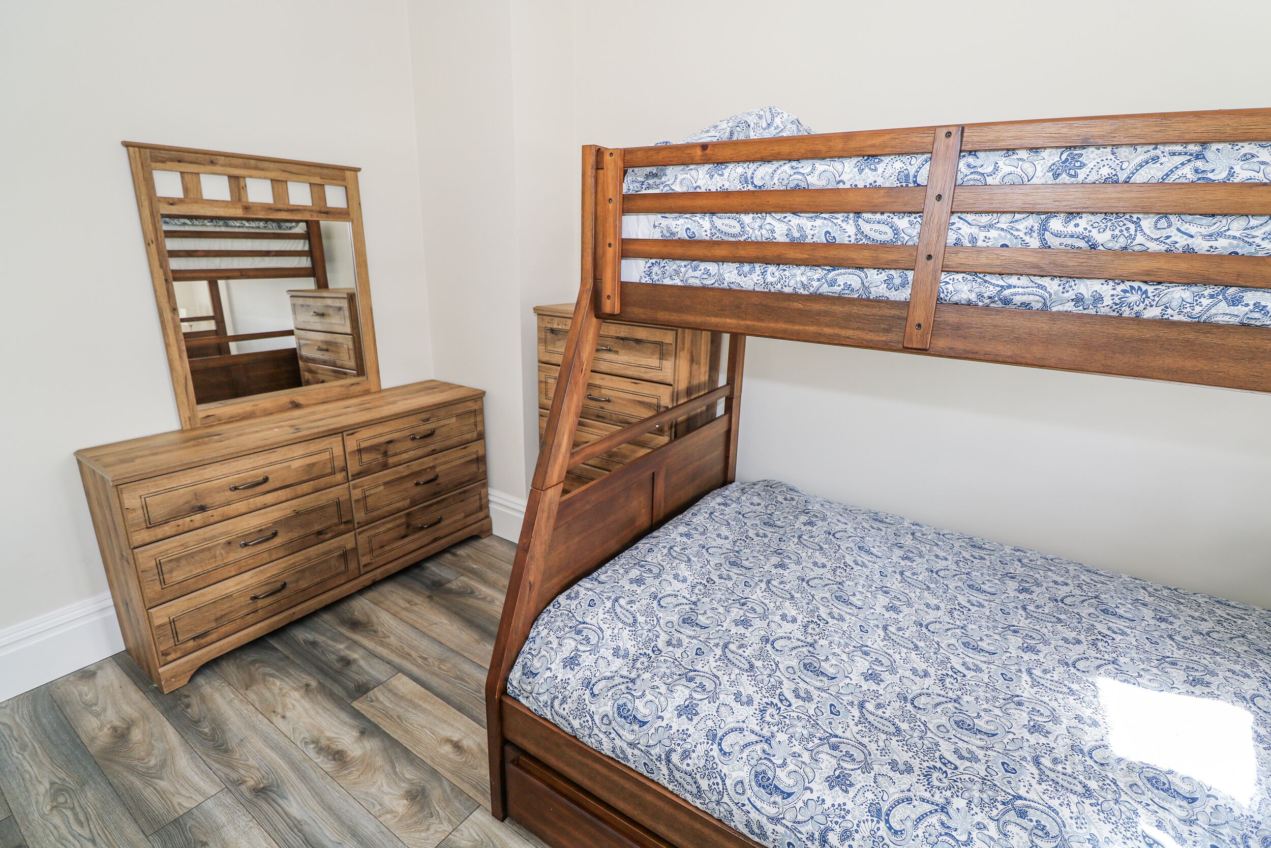 A bedroom with a wooden bunk bed, a dresser with drawers, and a mirror.