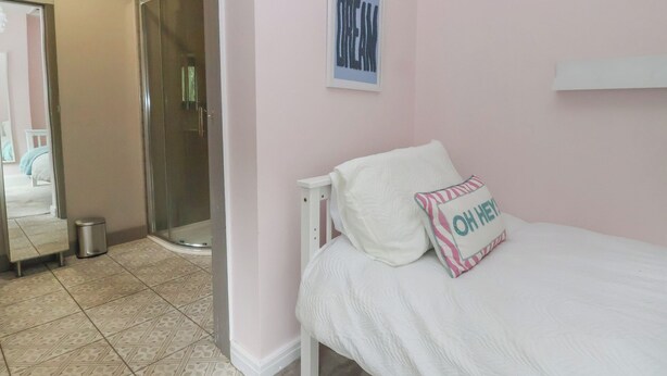 Quarto com cama, chuveiro e porta que dá para outro cômodo.