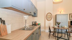 Una cocina moderna con encimera de madera, pileta de acero inoxidable y alacenas azules. Hay una zona de comedor con una mesa redonda y sillas.