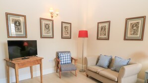 Un salón con televisor sobre un mueble de madera, un sillón a cuadros, un sofá beige con almohadones a cuadros y cuadros enmarcados en la pared.